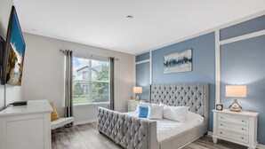 Une chambre à coucher avec un grand lit, deux tables de chevet, une commode, une fenêtre avec des rideaux et un tableau au mur.