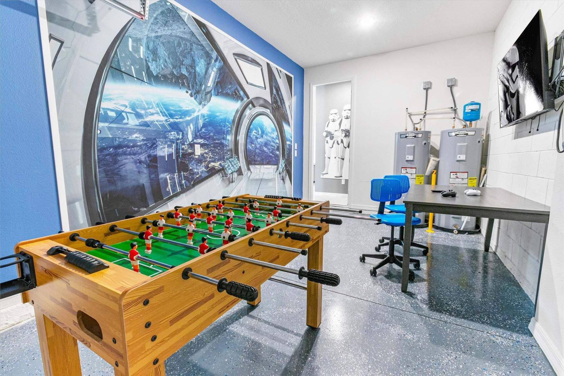 A room with a foosball table, a large mural, and a desk with computer equipment.