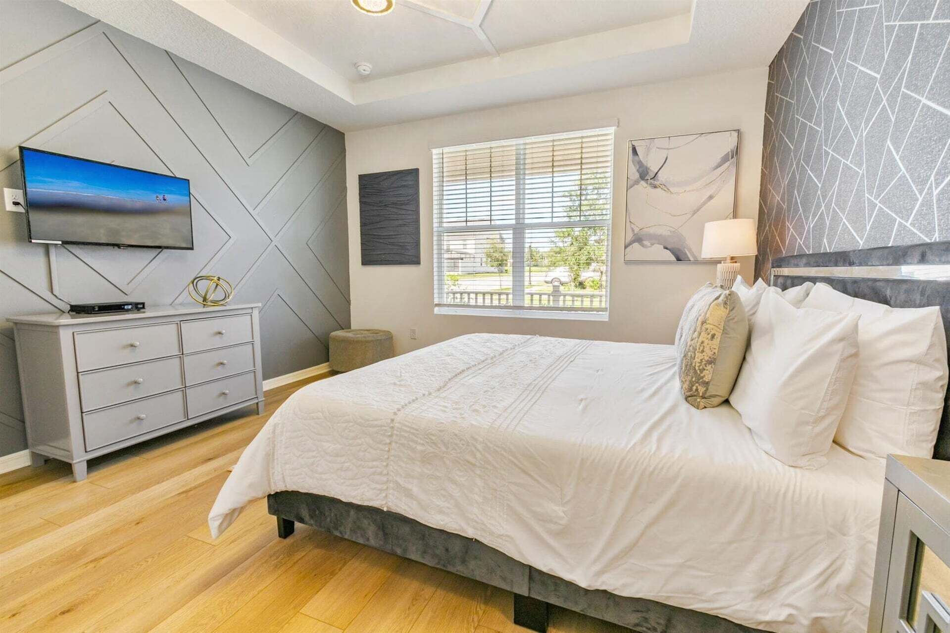 Een slaapkamer met een bed, een televisie, een dressoir en een raam met jaloezieën.