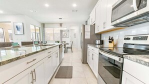 Une cuisine moderne avec des meubles blancs, un plan de travail en granit, des appareils électroménagers en acier inoxydable et un coin repas comprenant une table et des chaises.