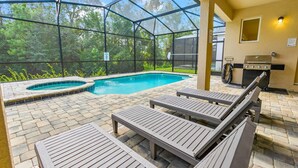 Un espace piscine comprenant un jacuzzi, des chaises longues et un barbecue.