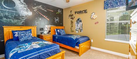 A bedroom with two wooden beds, a ceiling fan, Star Wars-themed wall art, and a window with blinds.