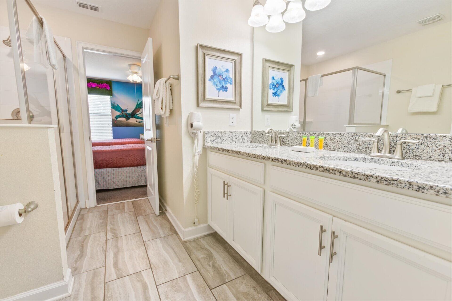 A bathroom with a large vanity, a shower, and a door leading to a bedroom.