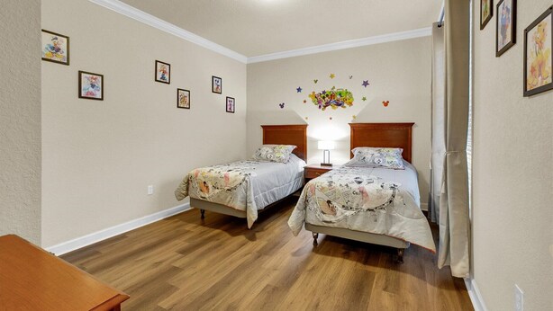 Ein Schlafzimmer mit zwei Betten, Holzboden und Wanddekorationen, darunter gerahmte Bilder und eine Wandsticker in Form eines Sterns.