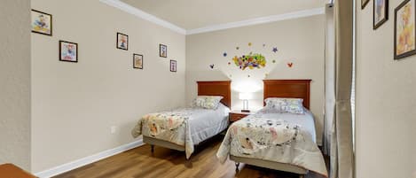 A bedroom with two beds, wooden flooring, and wall decorations including framed pictures and a star-shaped wall decal.