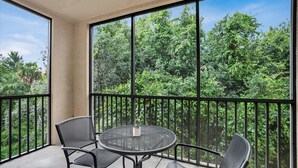 Ein Balkon mit rundem Tisch und zwei Stühlen, mit Blick auf einen üppigen, grünen Wald.