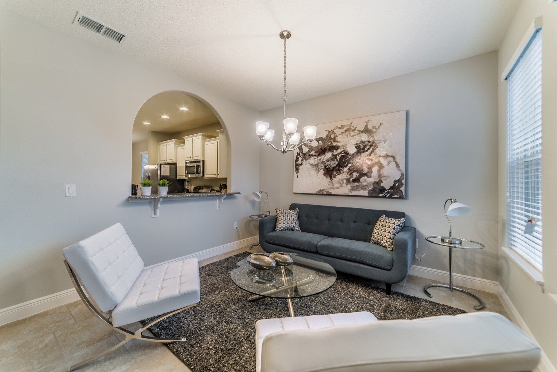 A modern living room with a grey sofa, a white armchair, a glass coffee table, and a large abstract painting on the wall.