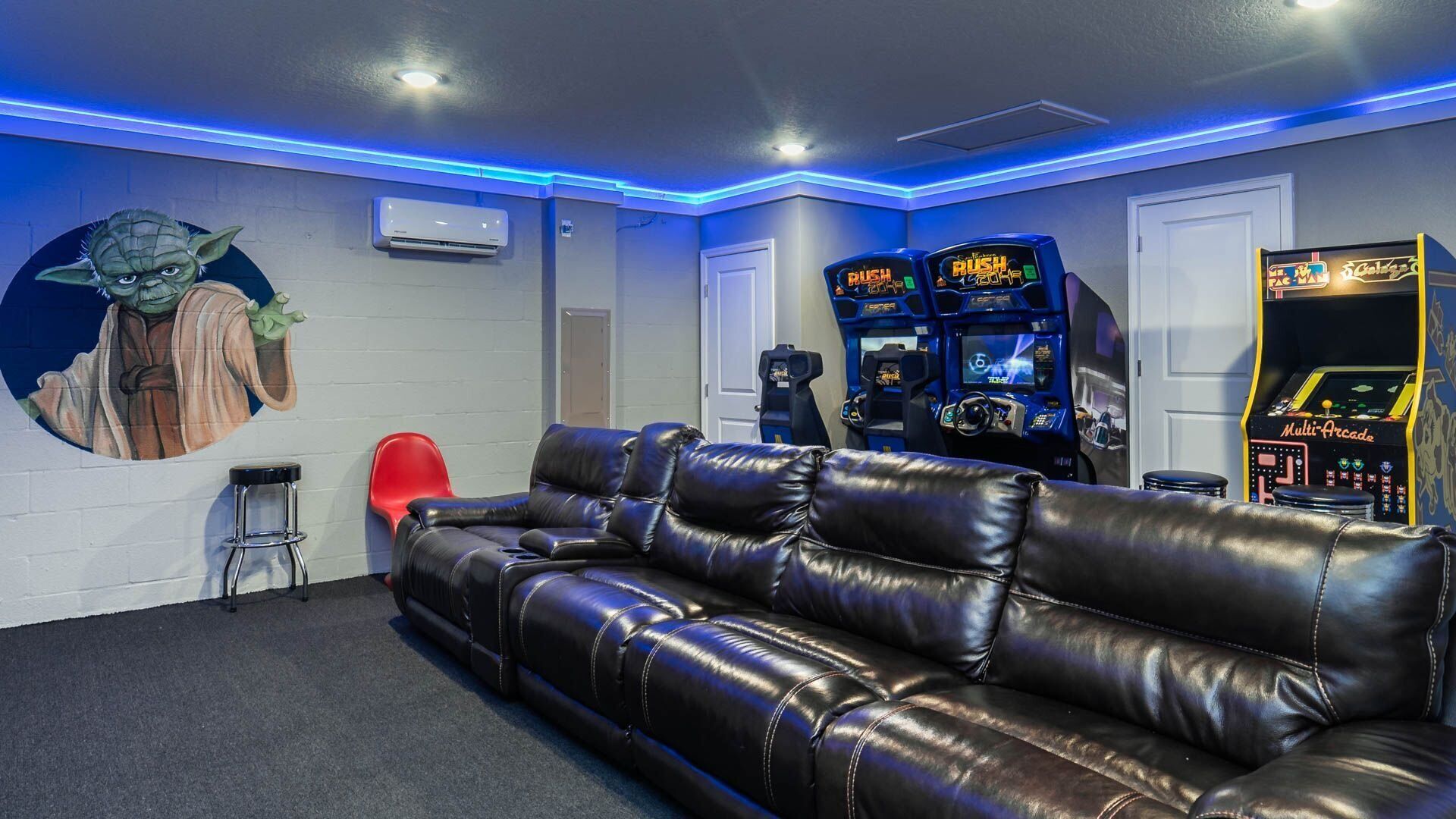 A room with a black leather couch, arcade games, and a wall mural.