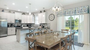 Una cocina moderna con armarios blancos, electrodomésticos de acero inoxidable y una zona de comedor con mesa de vidrio y sillas de madera.