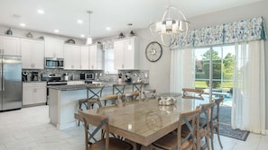 A modern kitchen with white cabinets, stainless steel appliances, and a dining area with a glass table and wooden chairs. - Hzd9057 (Davenport)