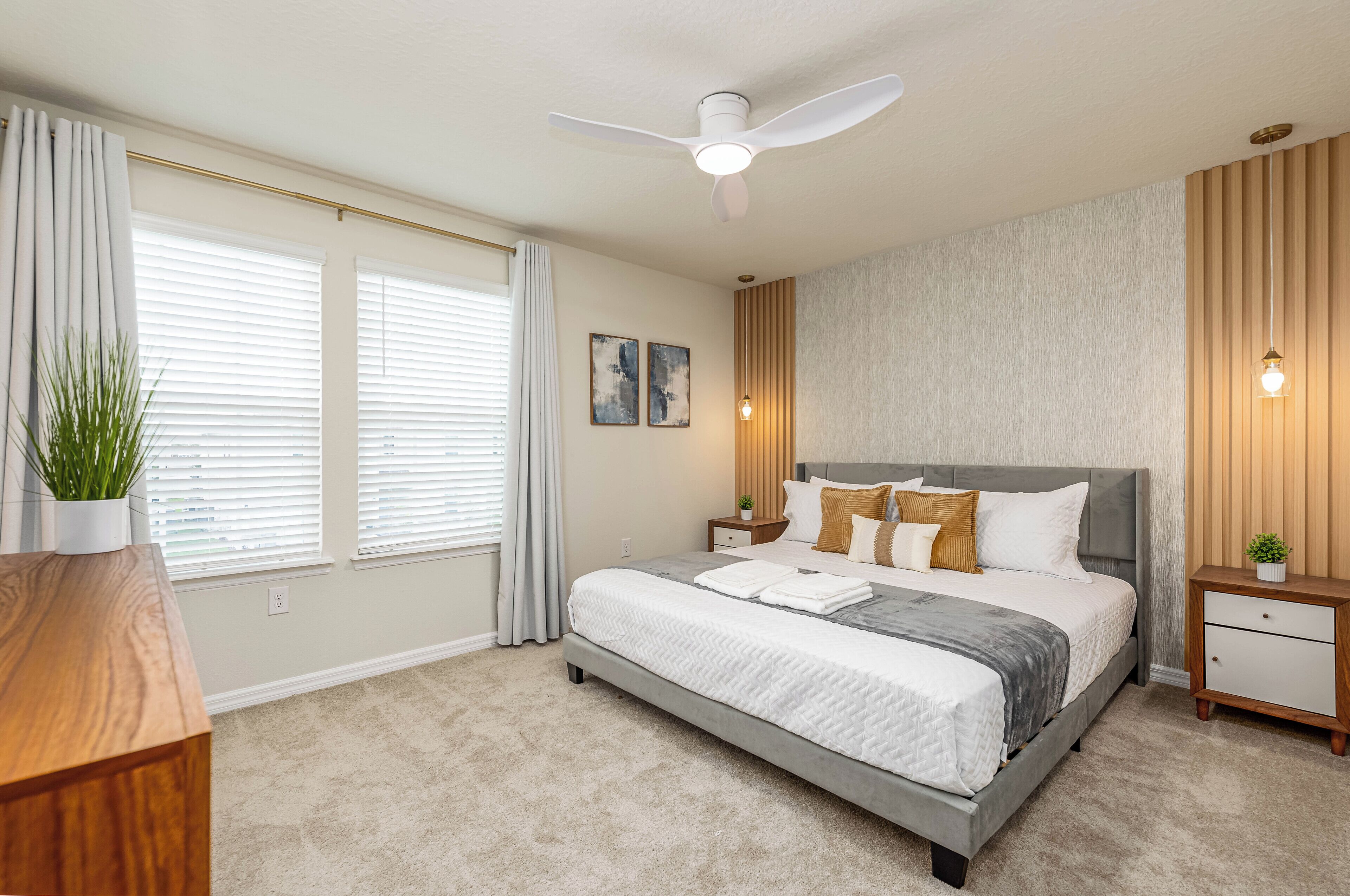 A modern bedroom with a large bed, a ceiling fan, bedside tables, and a nightstand.