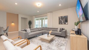 A modern living room with a sectional sofa, a coffee table, a TV mounted on the wall, and a desk with a lamp. - Special Offer Brand New Villa With Themed Rooms (Clermont)