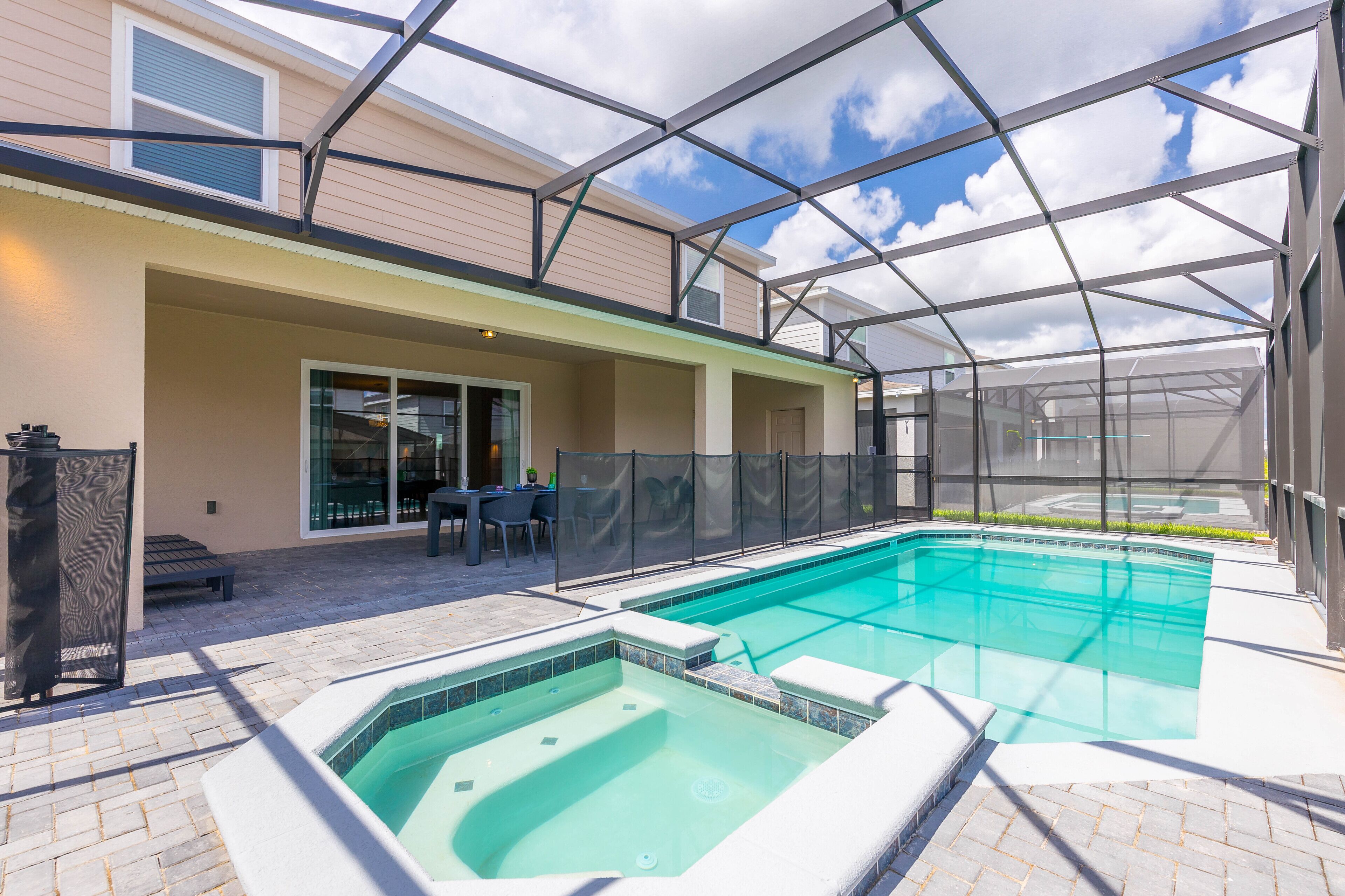 A swimming pool with a glass enclosure, a patio area with outdoor furniture, and a covered seating area.