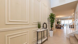 A hallway with a marble console table, potted plants, and a staircase leading to a dining area. - Special Offer Brand New Villa With Themed Rooms (Clermont)