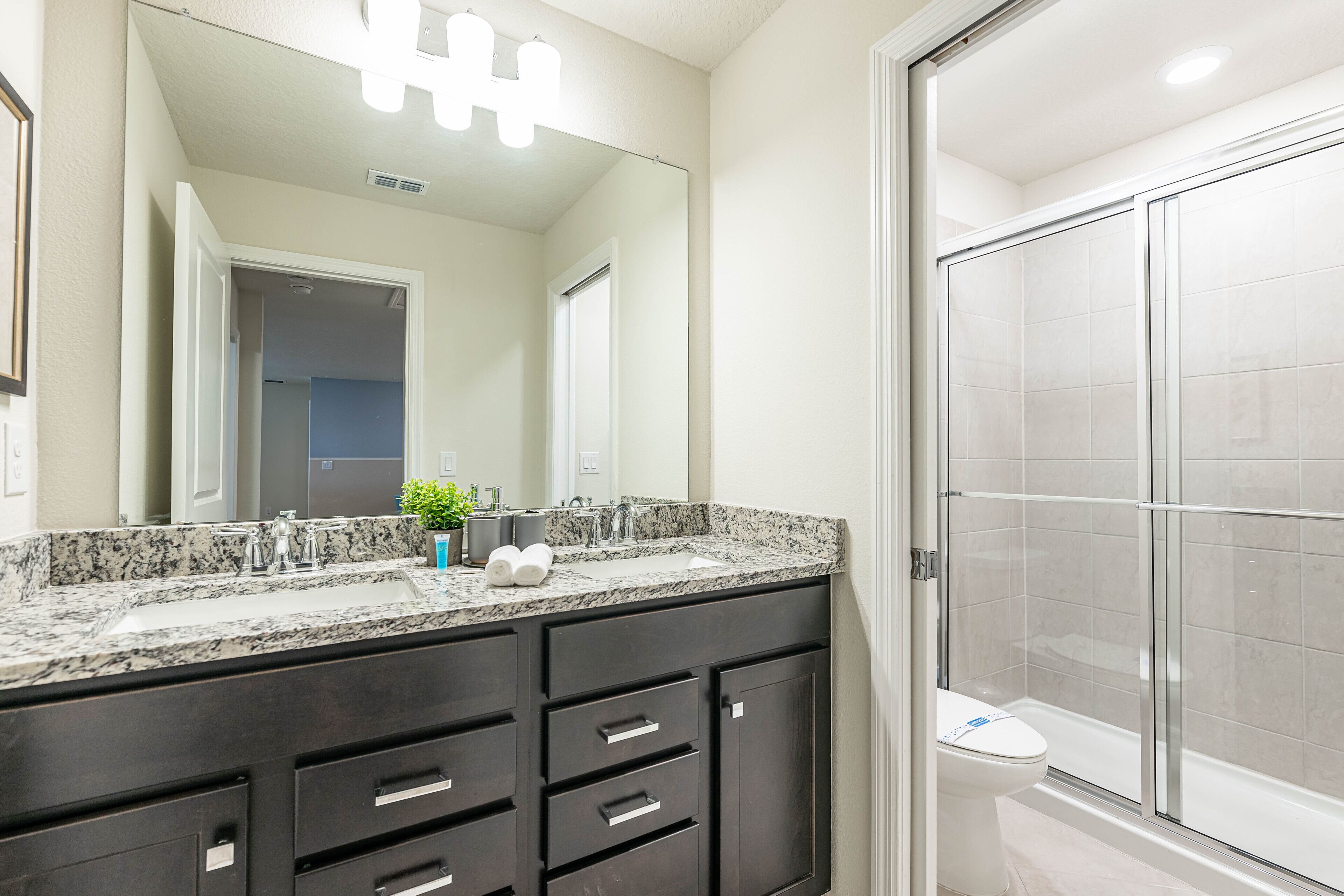 A bathroom with a double sink vanity, a mirror, a shower enclosure, and a toilet.
