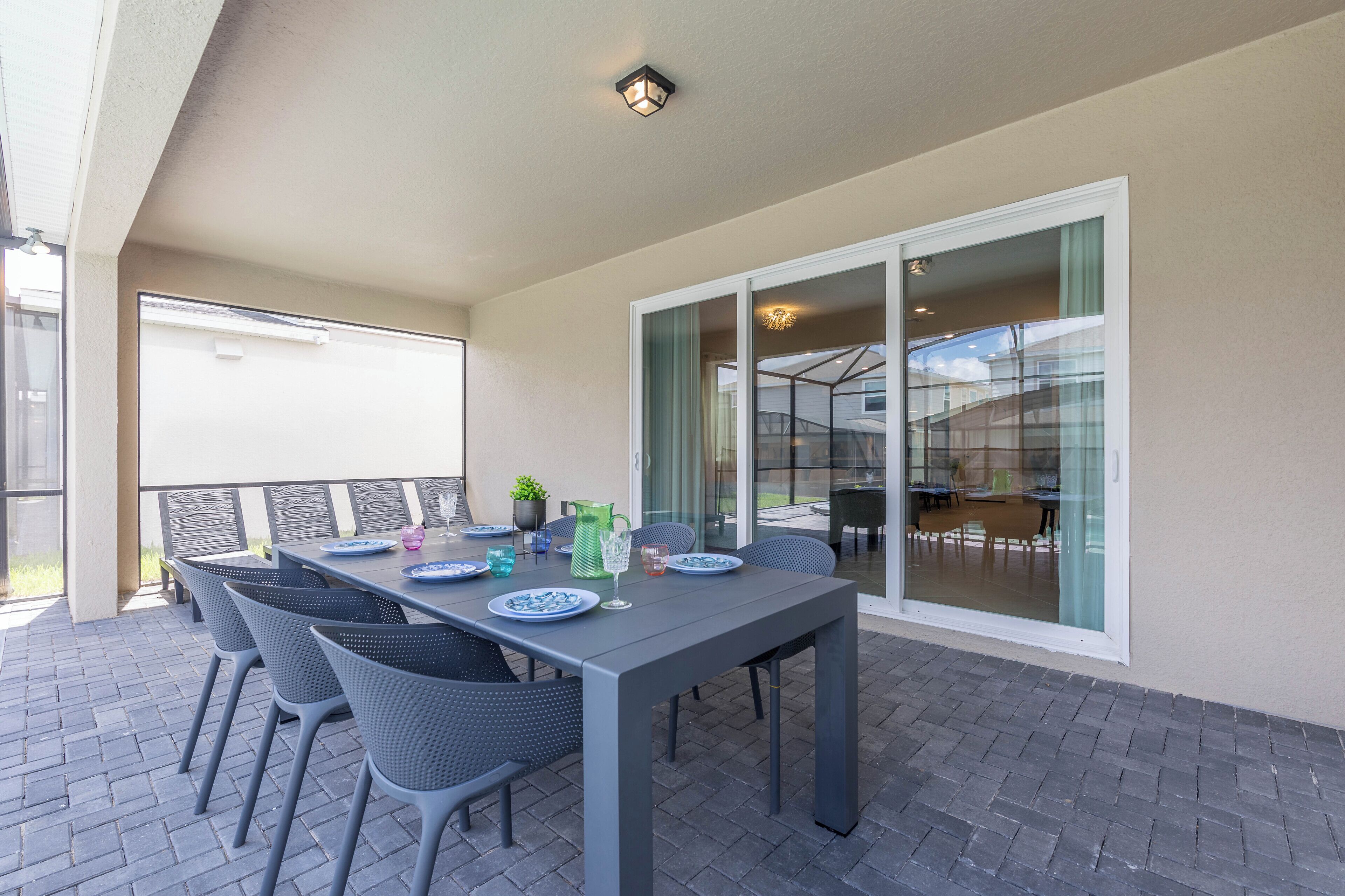 Un patio al aire libre con una mesa lista para comer, rodeado de sillas y una puerta de vidrio que da a un espacio interior.