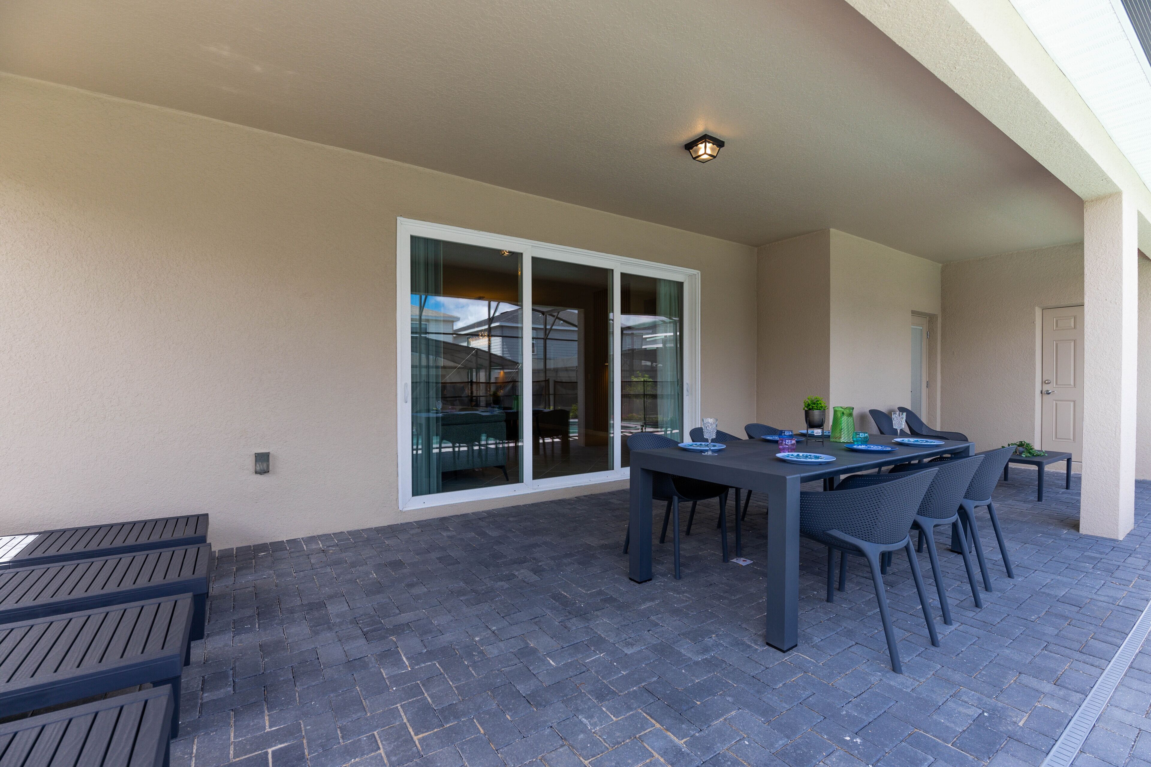Une terrasse extérieure avec une table et des chaises, une porte-fenêtre coulissante et une porte donnant sur l’intérieur.