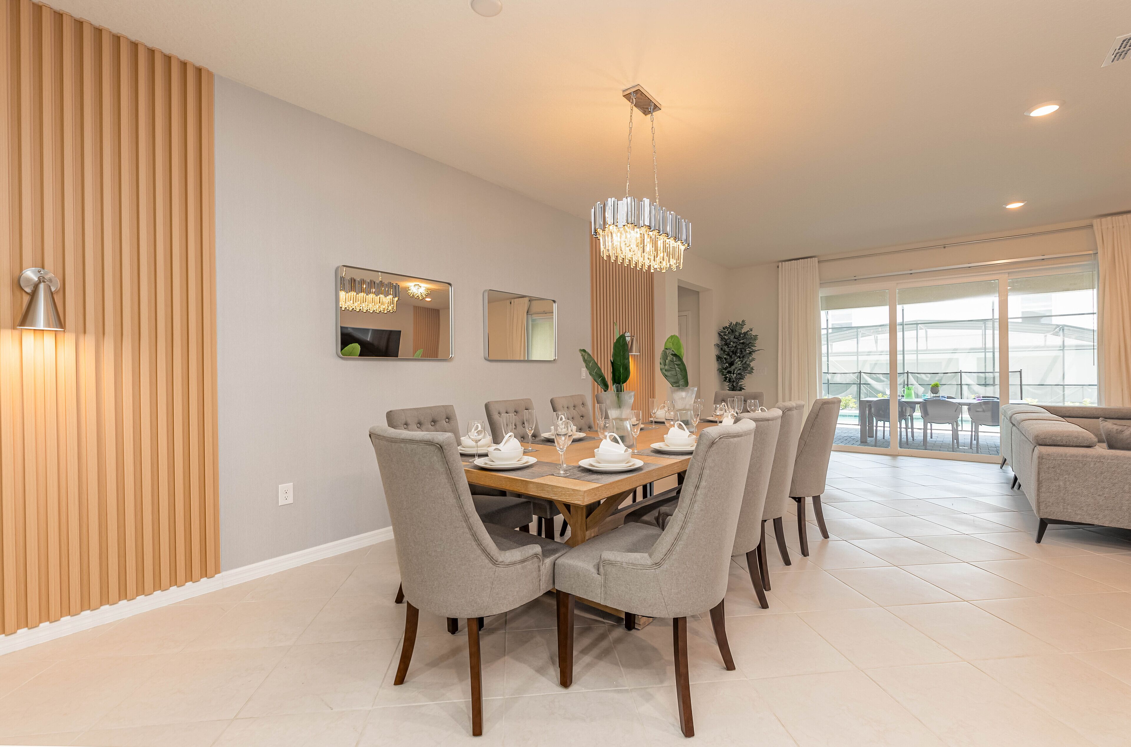 A modern dining area with a wooden table set for six, surrounded by grey upholstered chairs.