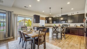 A modern kitchen with dark wood cabinets, a large island, and a dining area with a wooden table and chairs. - Spacious Family Getaway Near Downtown (Fountain)