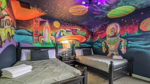 Une chambre avec deux lits, une table de chevet et une fresque murale représentant un thème spatial avec des planètes et une soucoupe volante.