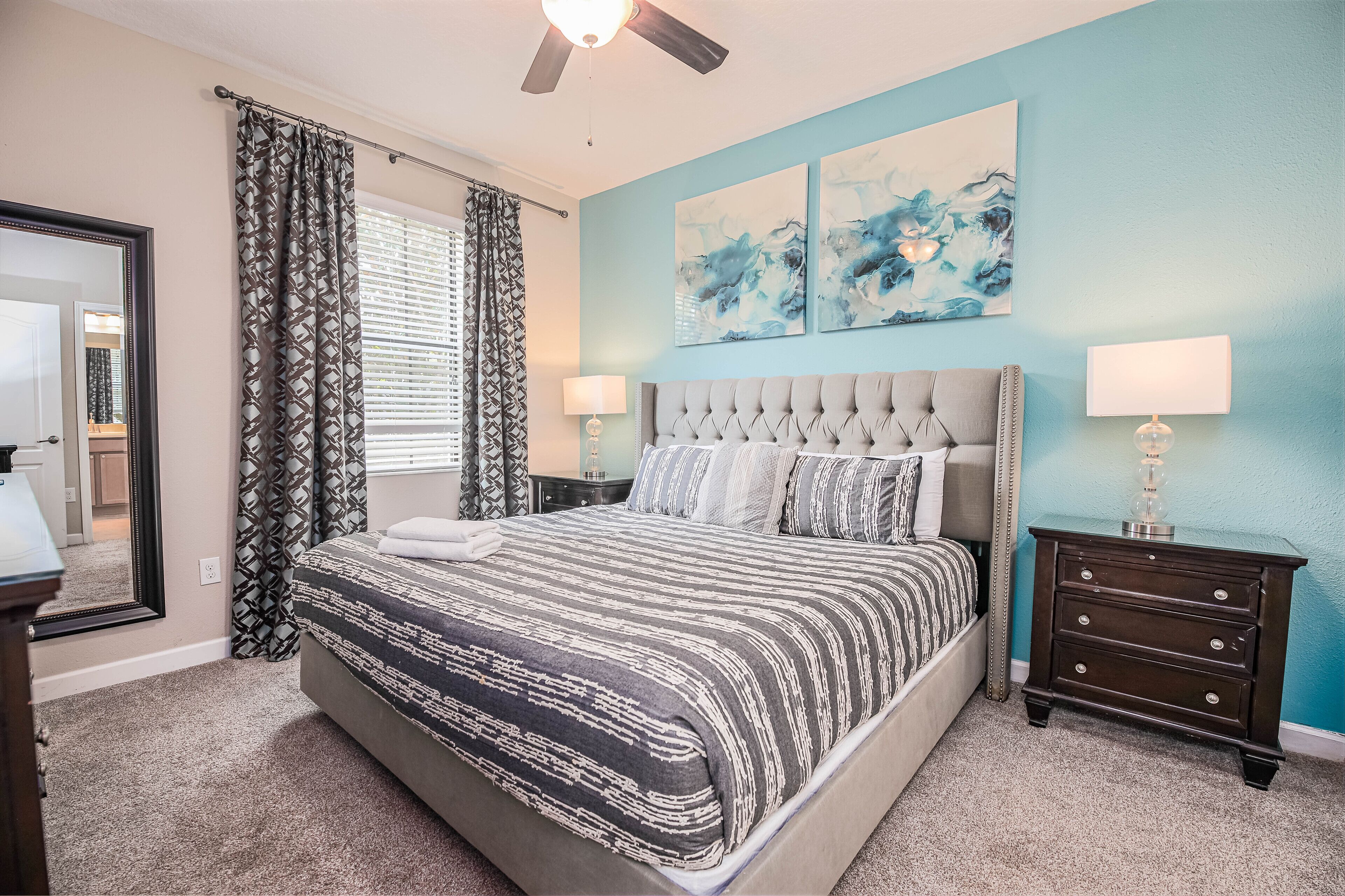 A bedroom with a large bed, two bedside tables, a ceiling fan, and artwork on the wall.