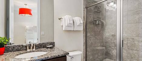 A bathroom with a double sink, a toilet, a glass shower enclosure, and a red pendant light.