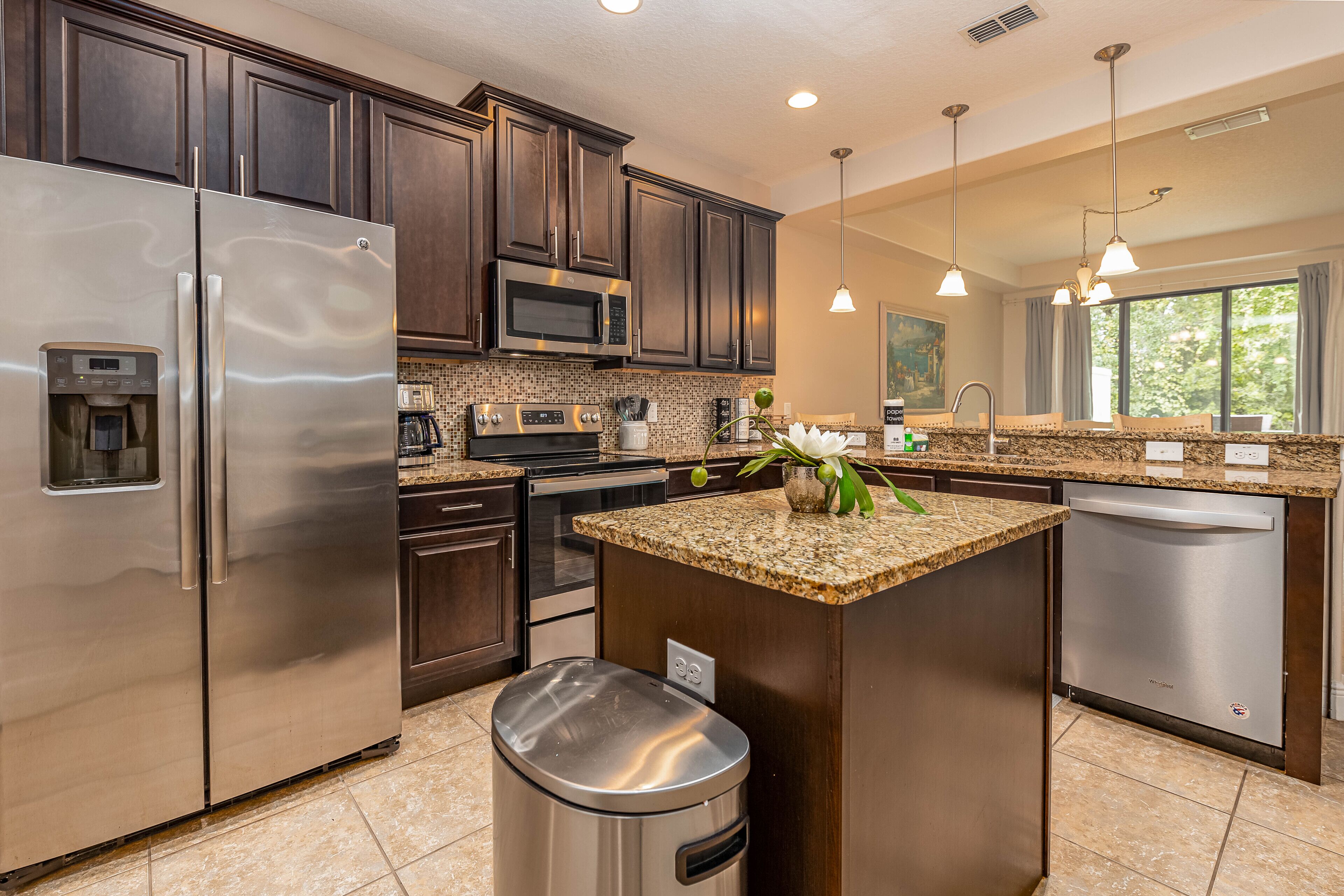 A modern kitchen with stainless steel appliances, dark wood cabinets, granite countertops, and pendant lighting.