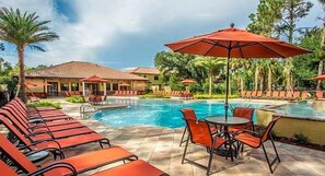 A pool area with lounge chairs and umbrellas, surrounded by palm trees and a building with a tiled roof. - Tvpm-8079br/fcg (Davenport)