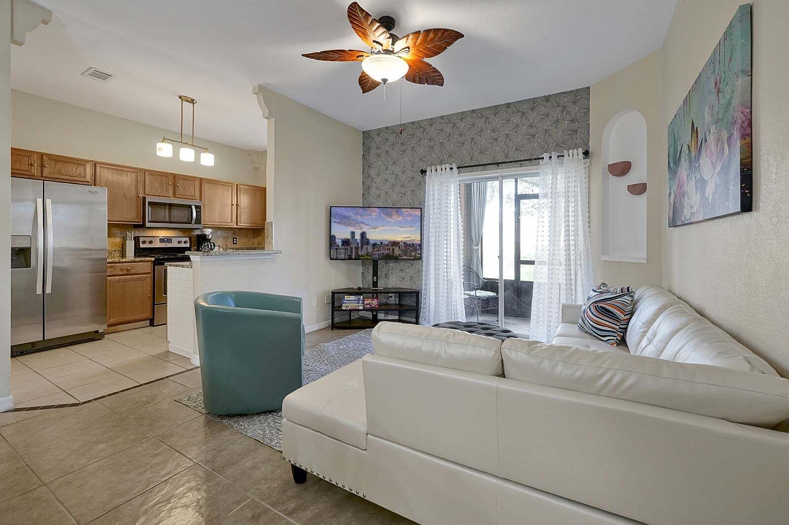 Un salon moderne avec un canapé blanc, un fauteuil turquoise, un téléviseur à écran plat et un ventilateur de plafond.