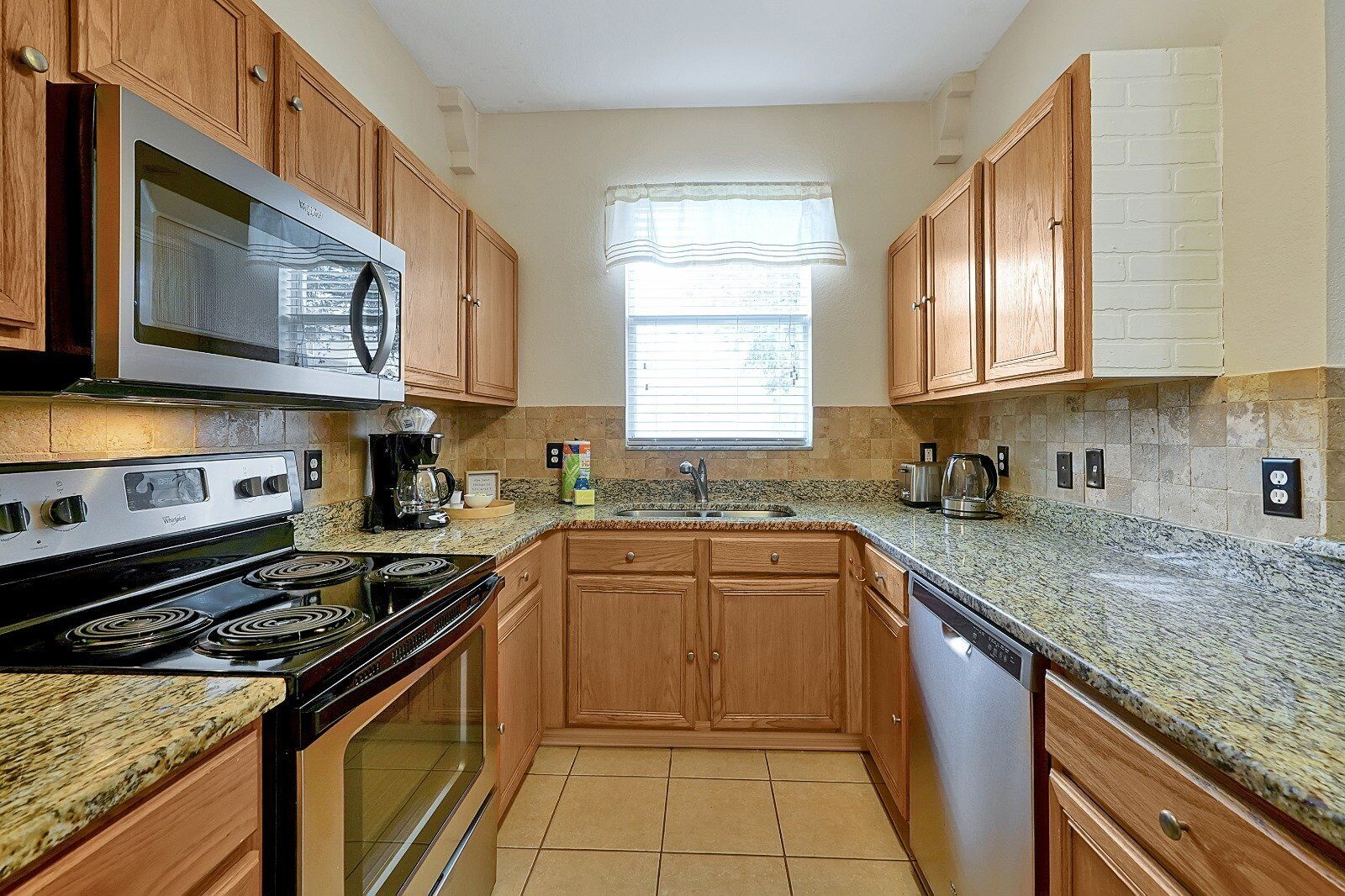 A kitchen with wooden cabinets, a microwave, stove, and granite countertops.