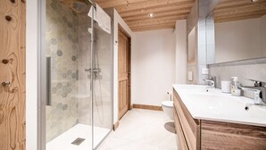 Un baño moderno con cabina de ducha de vidrio, techo de madera y lavamanos blanco con espejo.