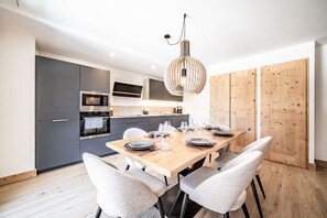 A modern kitchen with grey cabinets, a wooden dining table set for six, and a hanging light fixture. - CHALET PASCAL B101: New 3 bedrooms for 6 people (MORZINE)