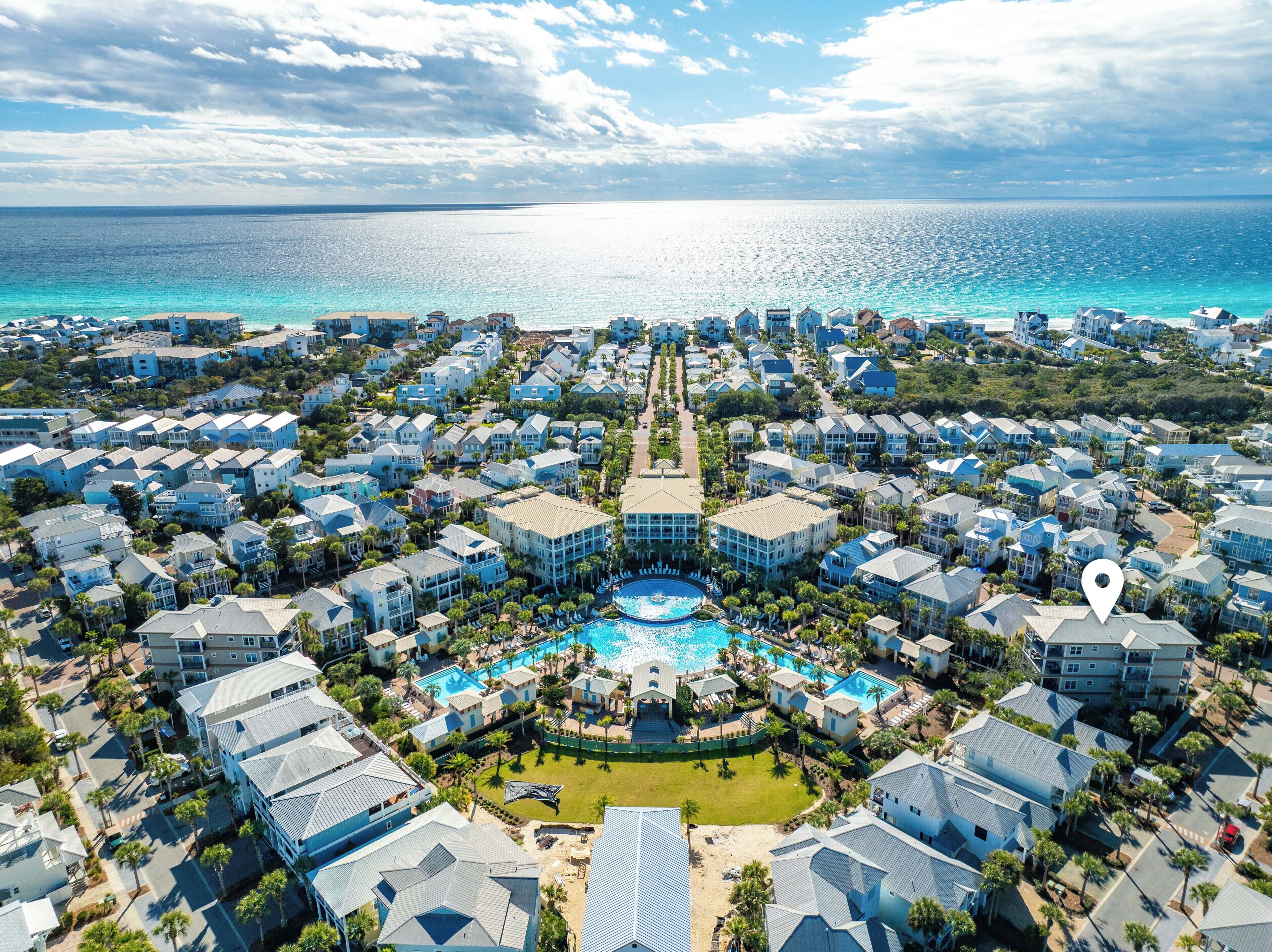 A resort with multiple buildings, a central swimming pool, and a view of the ocean.