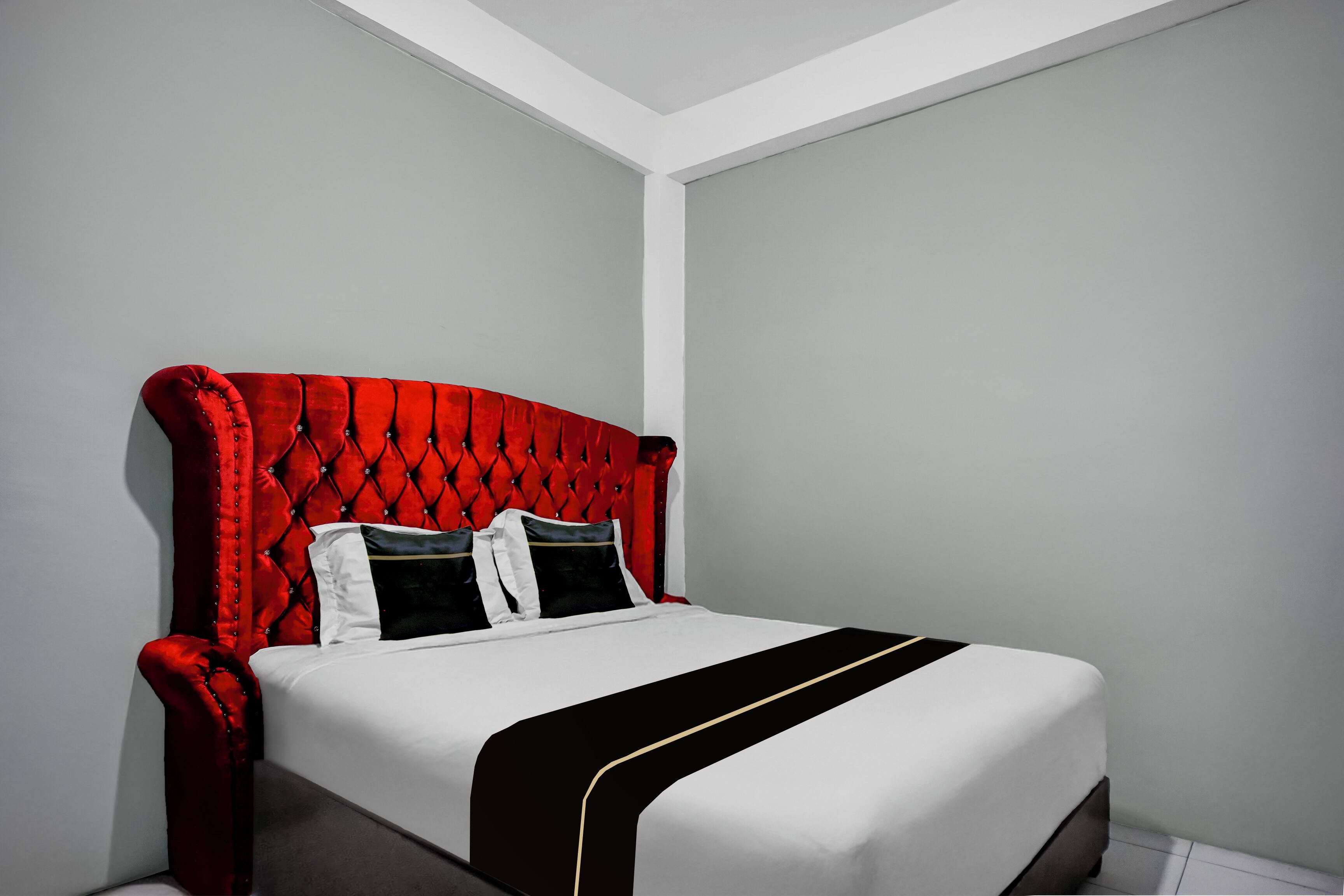 A neatly made bed with a red upholstered headboard, white bedding, and a black and gold accent.