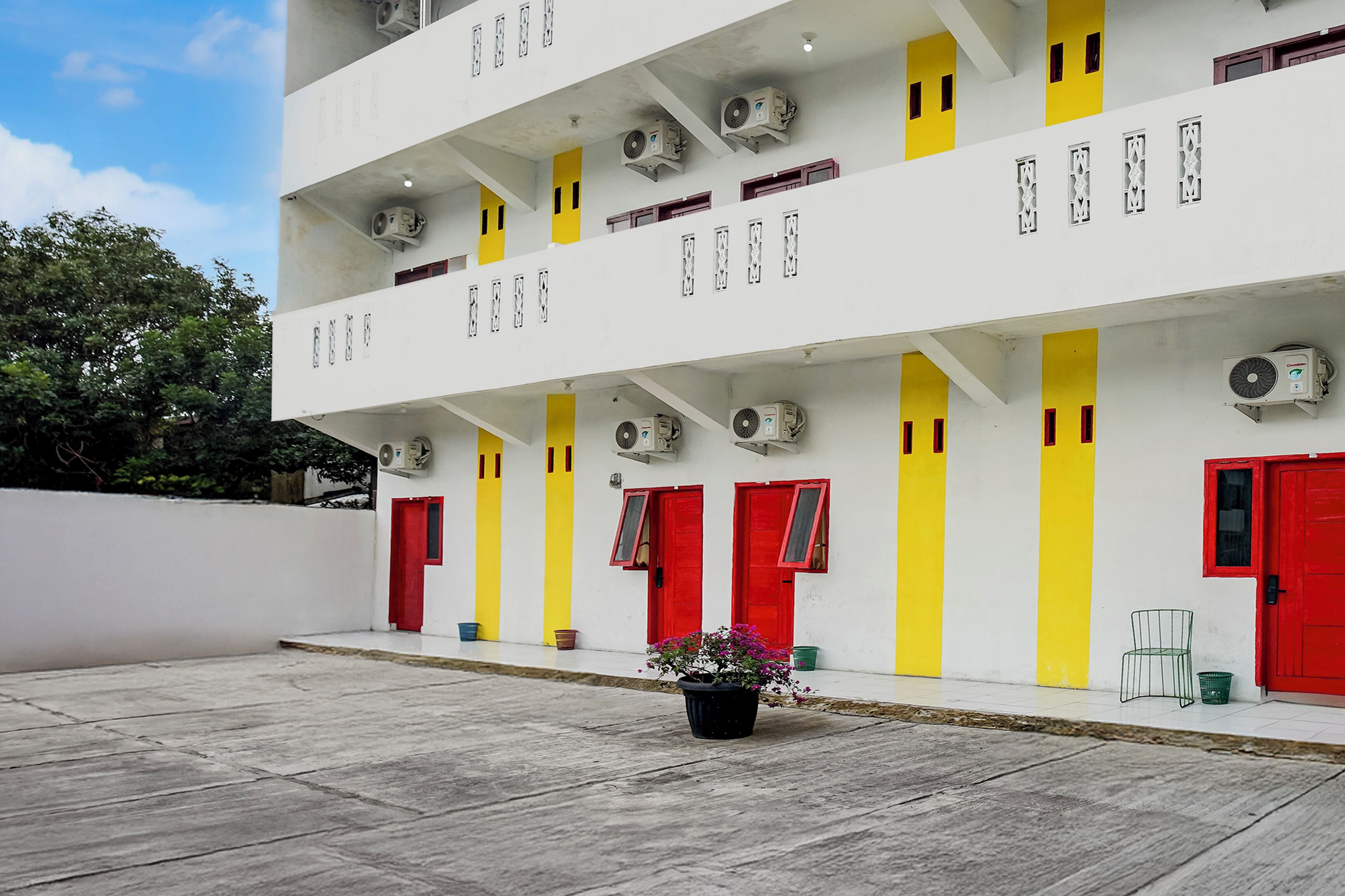A multi-story building with red and yellow doors, air conditioning units, and a potted plant in the courtyard.