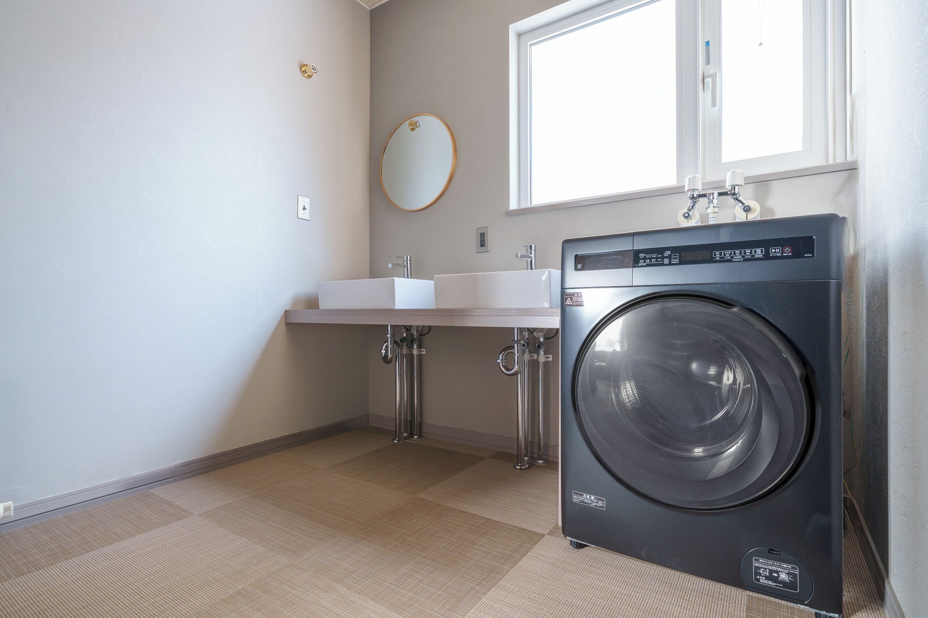 A laundry room with a front-loading washing machine, a sink, and a window above the sink.
