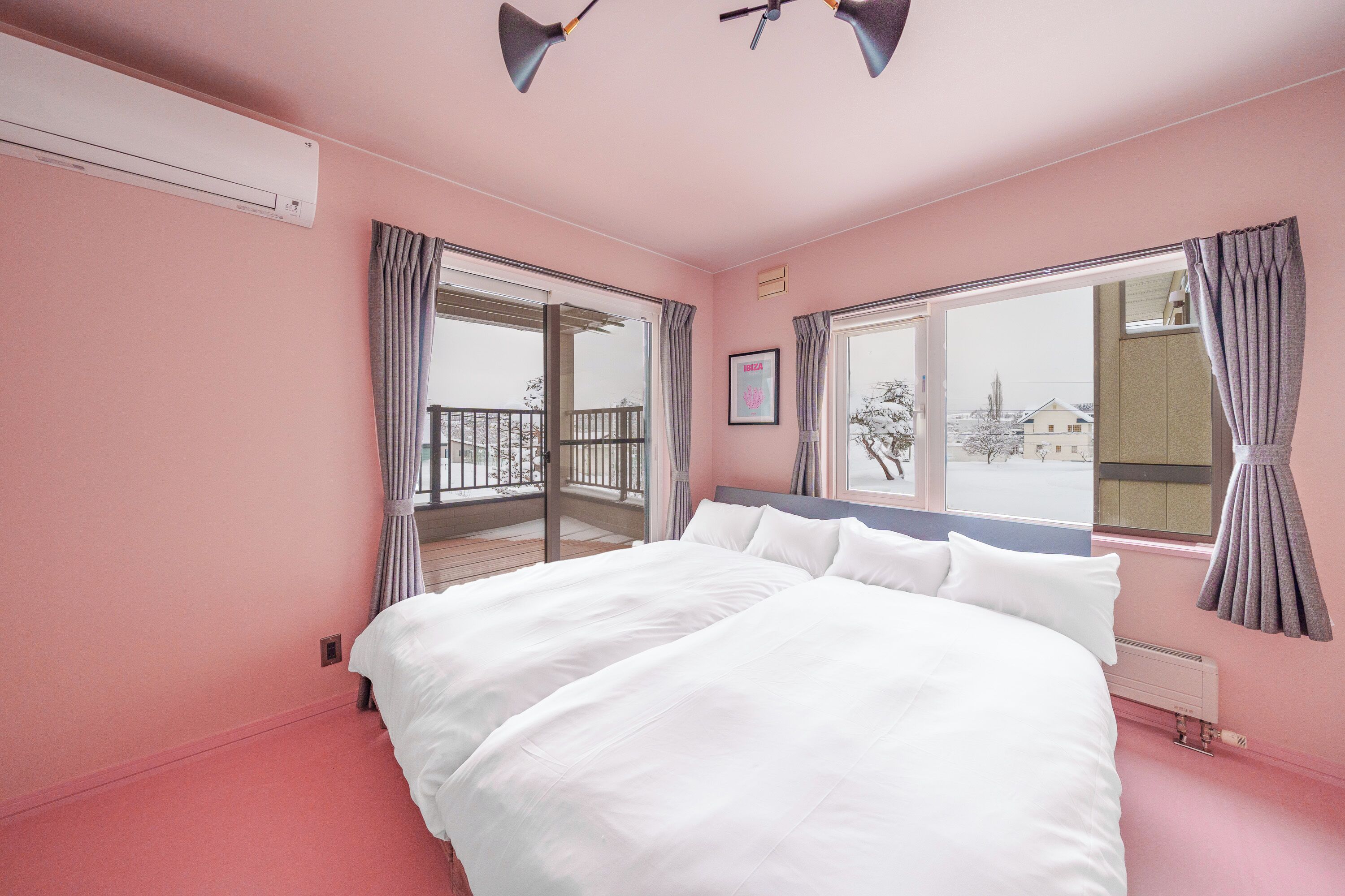 A pink-themed bedroom with a large bed, a balcony, and a view of the outside.