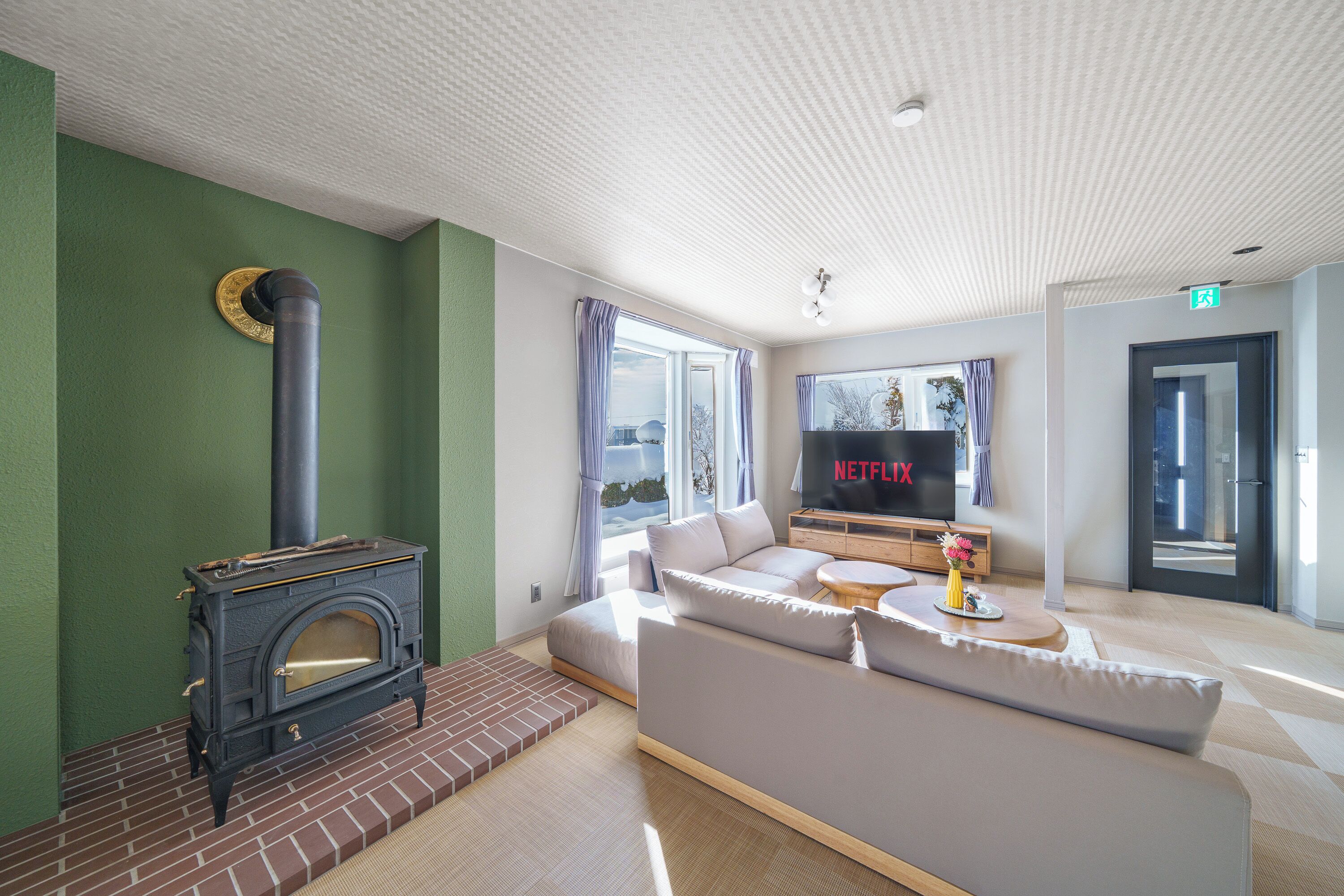 Ein modernes Wohnzimmer mit Kamin, einer Couch, einem Fernseher und Blick ins Freie.
