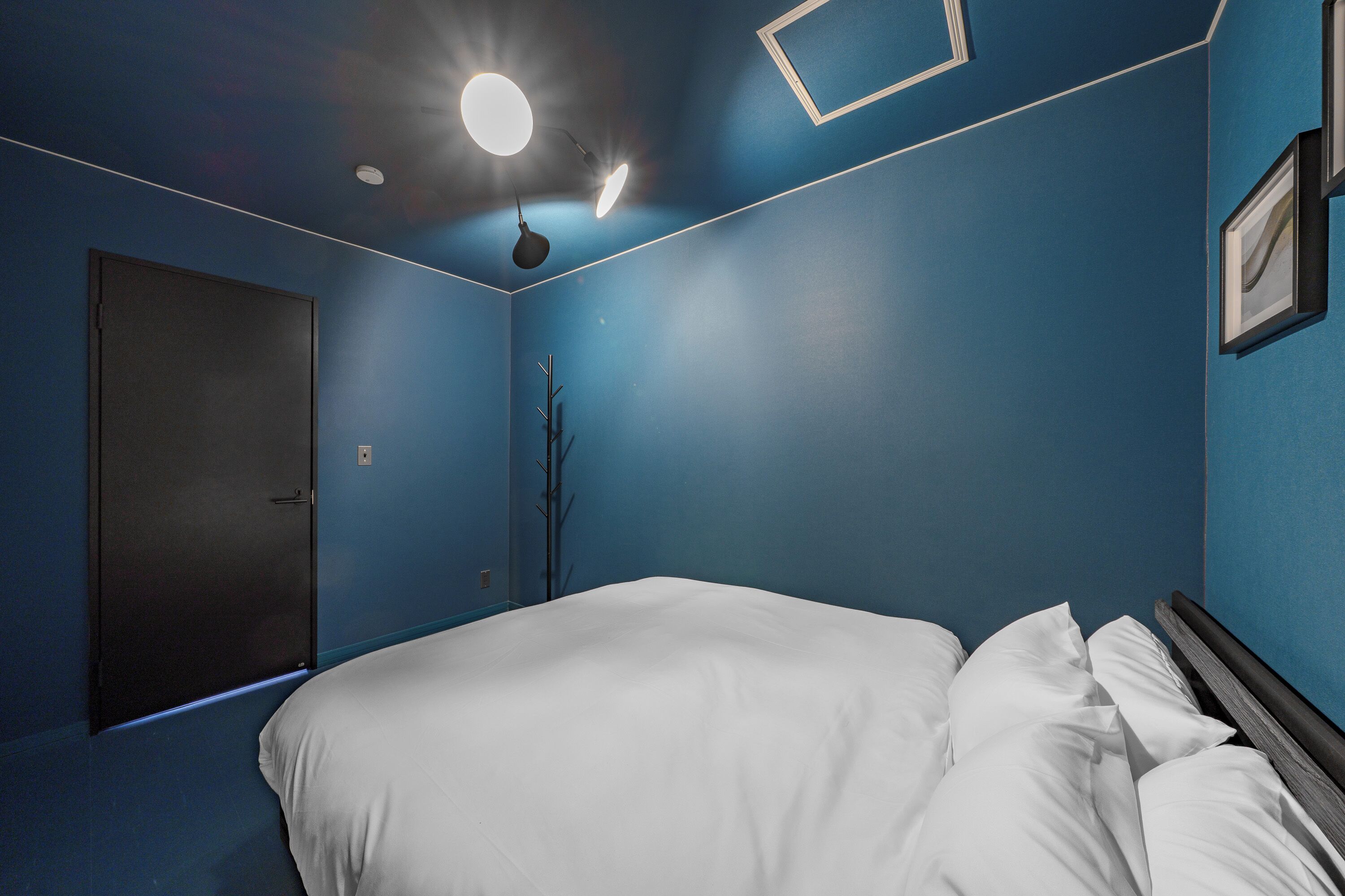 A bedroom with a bed, a door, and a wall-mounted light fixture.