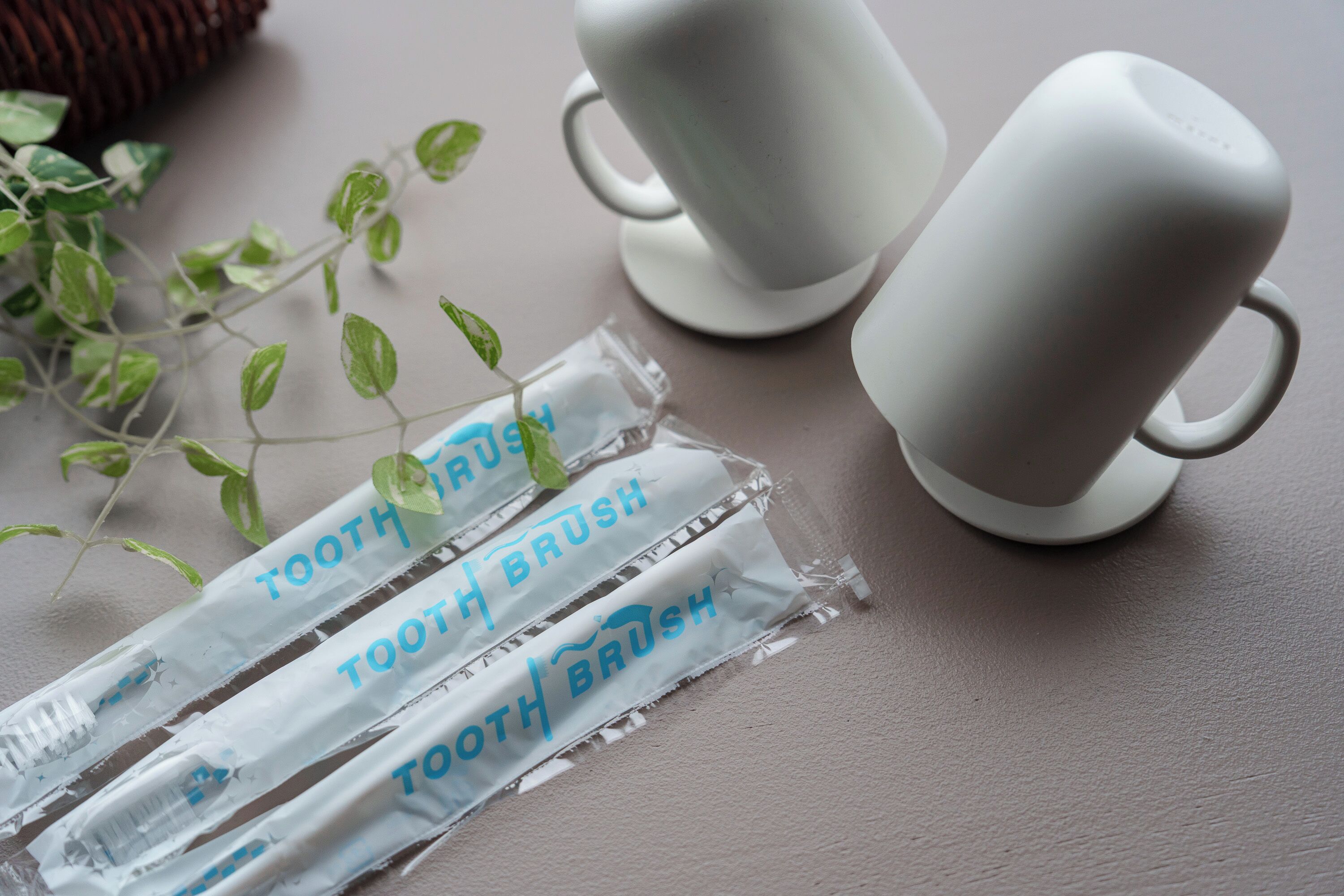 A table with three toothbrushes in clear packaging and two white ceramic cups.