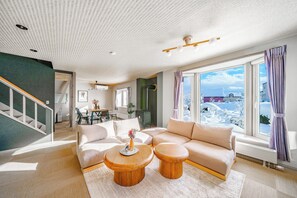 A spacious living room with a large window, a staircase, and a view of a snowy landscape. - THE CRANE SANCTUARY KAMIFURANO (Kamifurano)