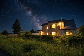 Una moderna casa a due piani con una scala esterna ben visibile, un'ampia finestra e interni luminosi.