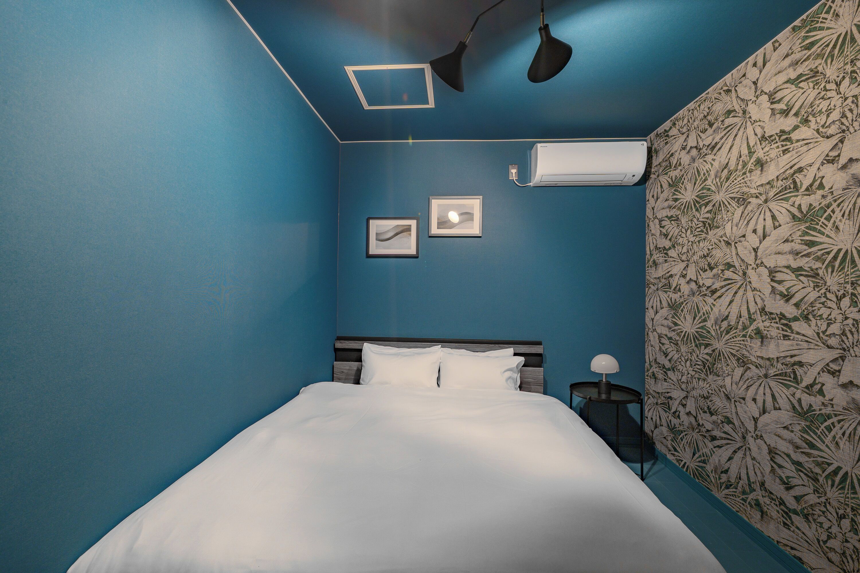 Ein Schlafzimmer mit einem Bett, einem Nachttisch, einer Lampe und zwei gerahmten Bildern an der Wand.