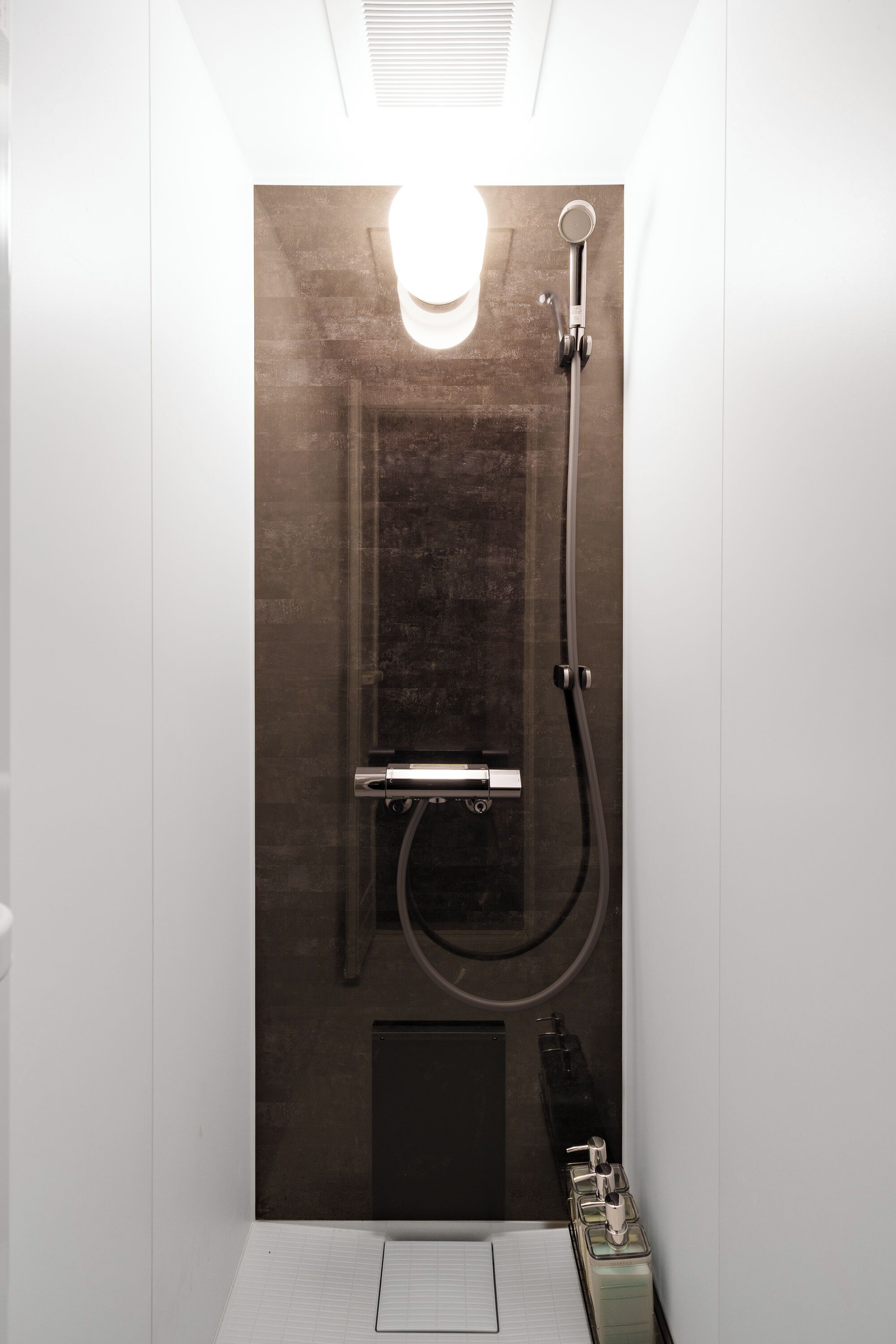 A small, enclosed shower area with a glass door, a handheld showerhead, and a wall-mounted faucet.