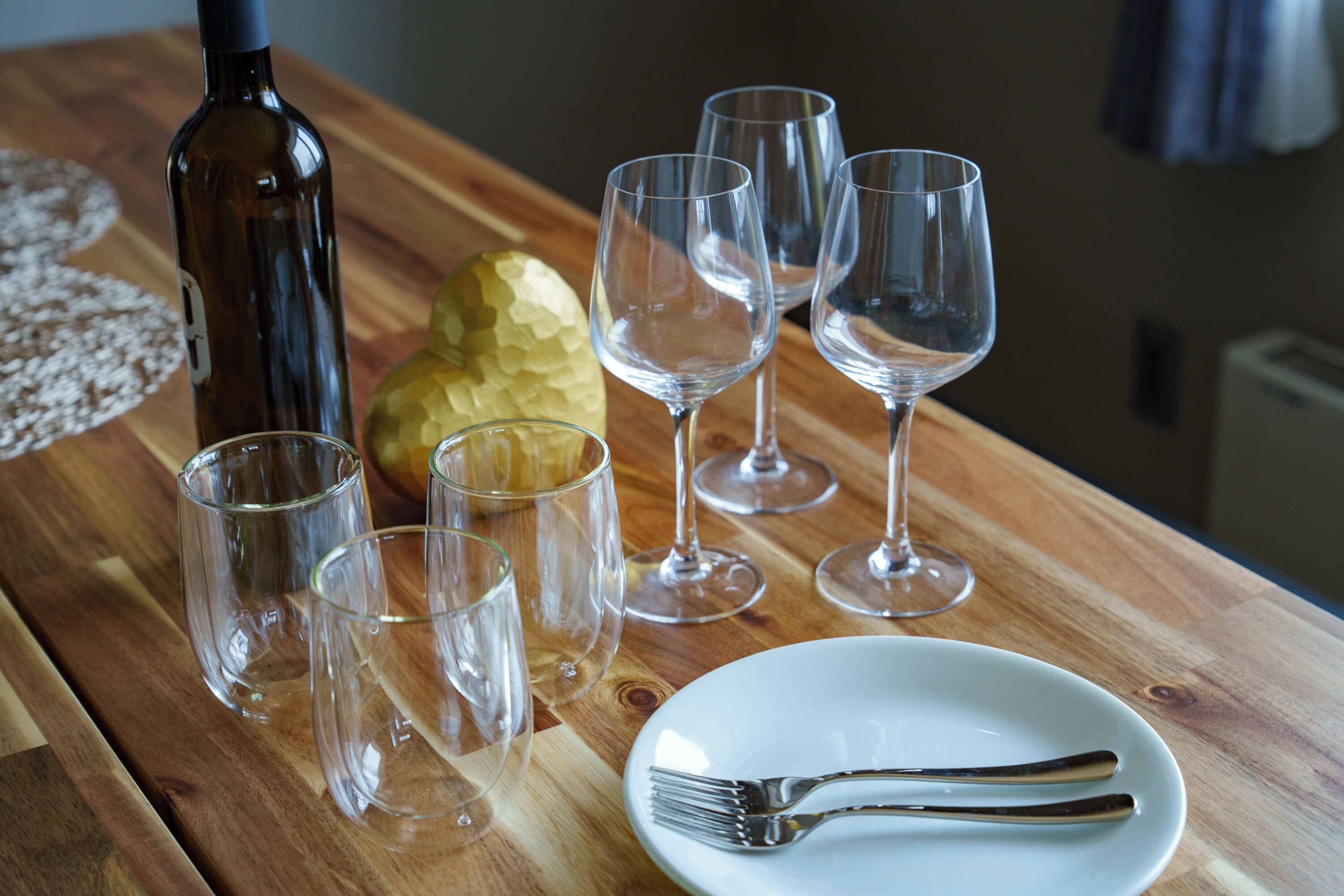 Une table en bois avec une bouteille, des verres à vin, une assiette avec une fourchette et un objet décoratif.