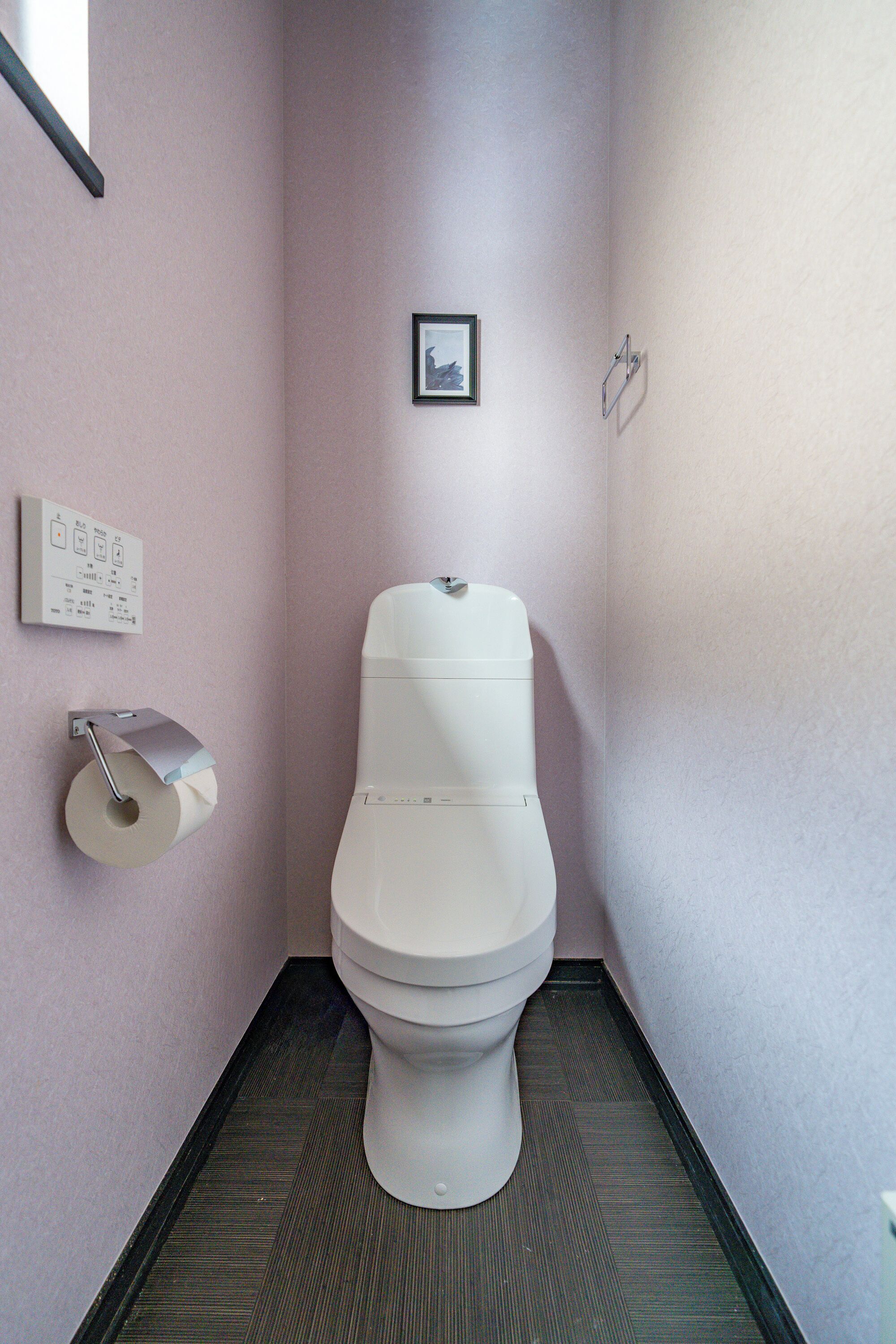 A small, narrow bathroom with a toilet, a toilet paper holder, and a framed picture on the wall.