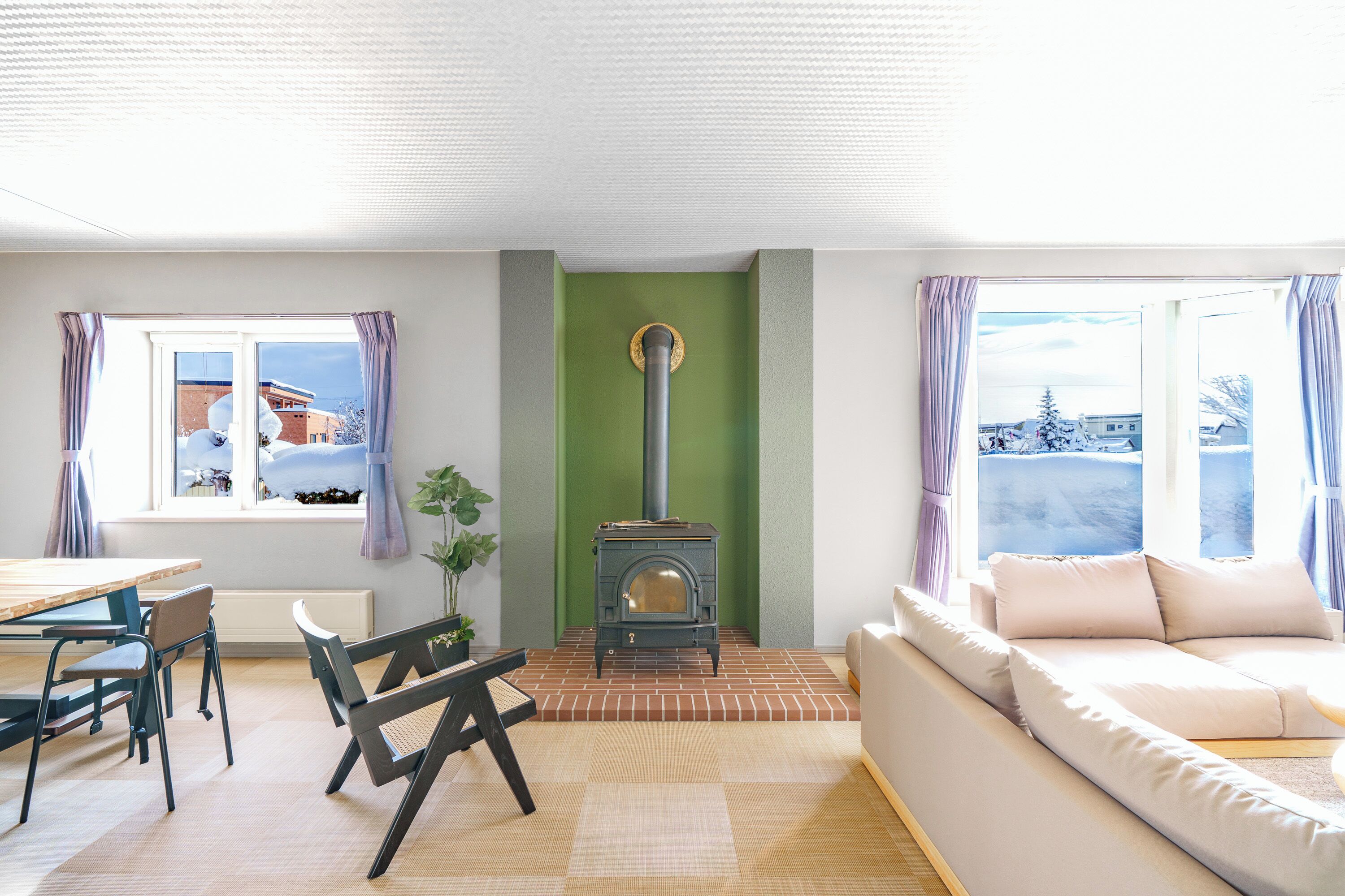 A cozy living room with a fireplace, a sofa, a dining table with chairs, and a view of the outside.