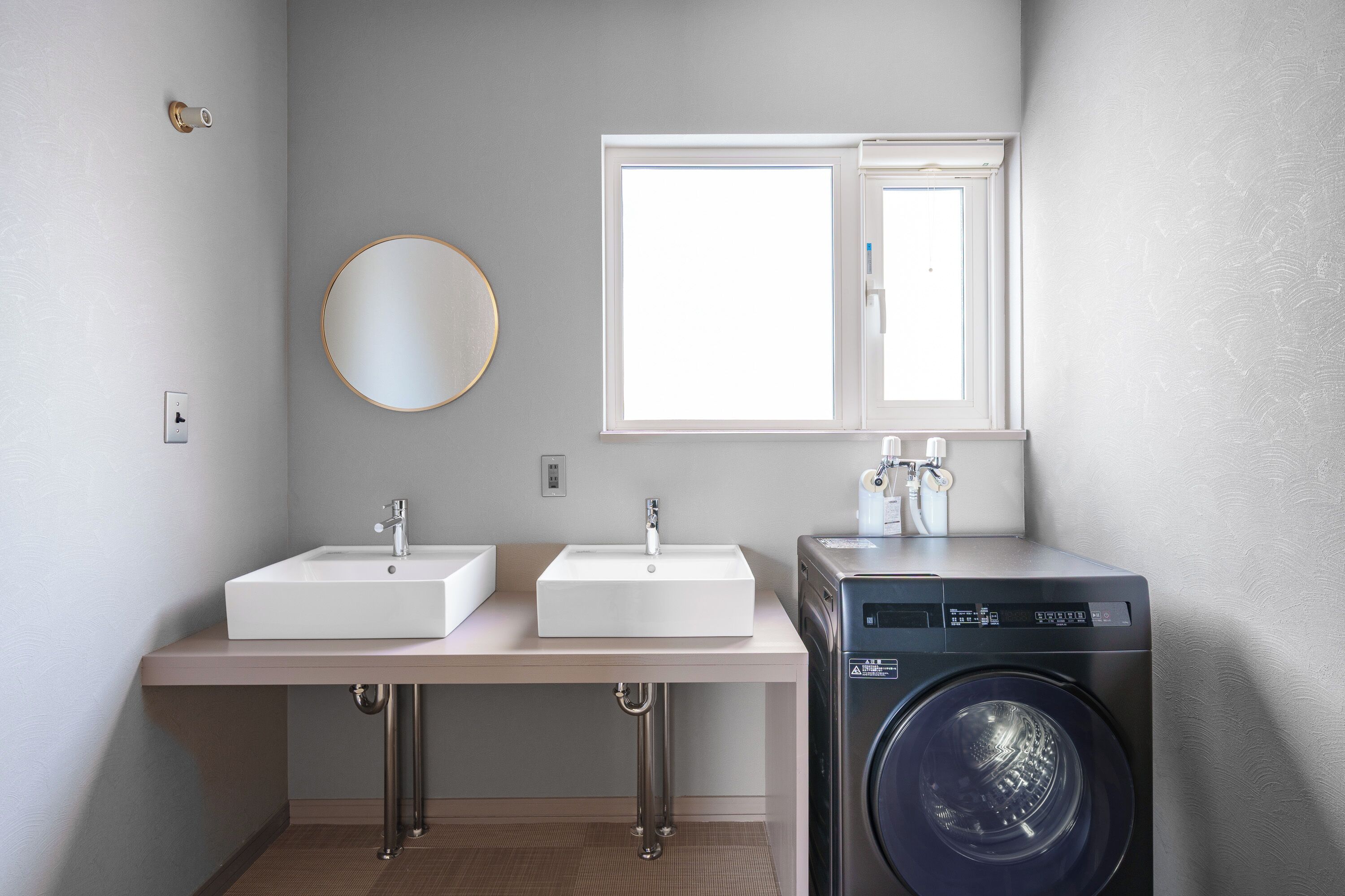 A modern bathroom with two sinks, a mirror, a window, and a washing machine.