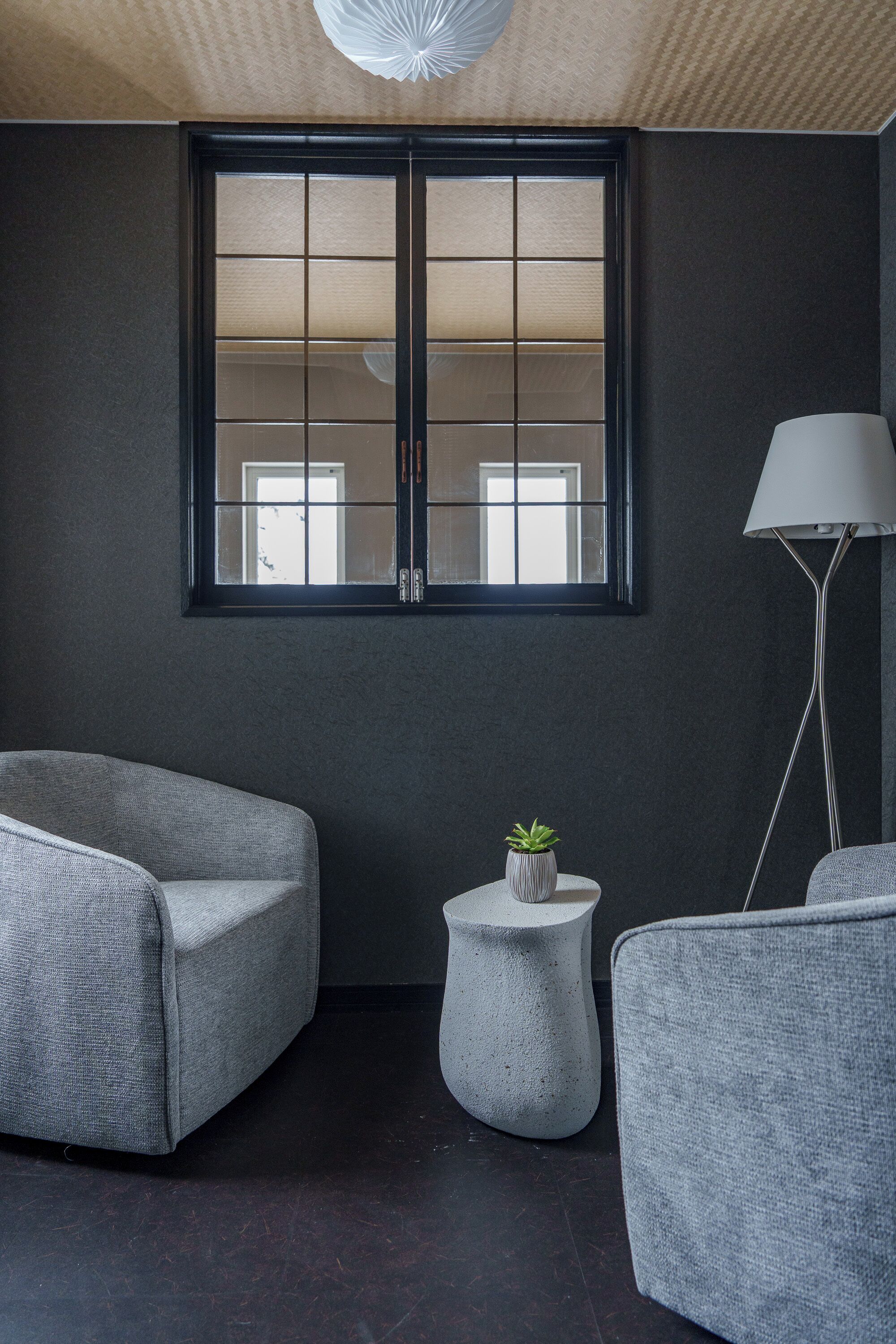 A modern room with a large window, two grey armchairs, a small round table with a plant, and a floor lamp.