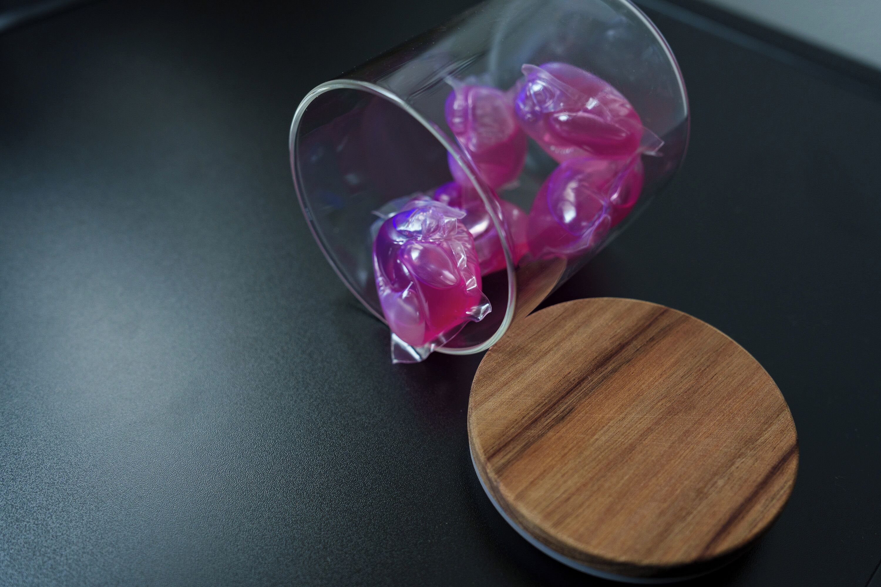 A glass container with purple items on a black surface next to a wooden lid.